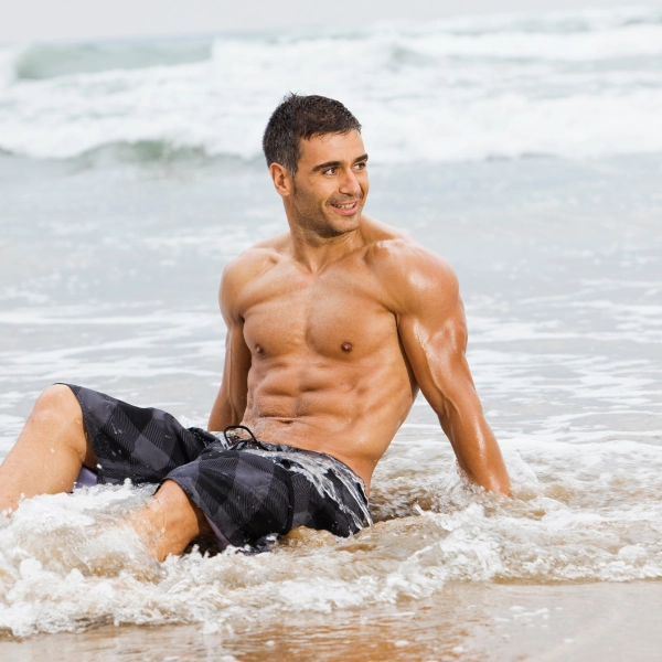 Fit, shirtless man on beach shows toned physique, after Male BHRT in Powell, WY.