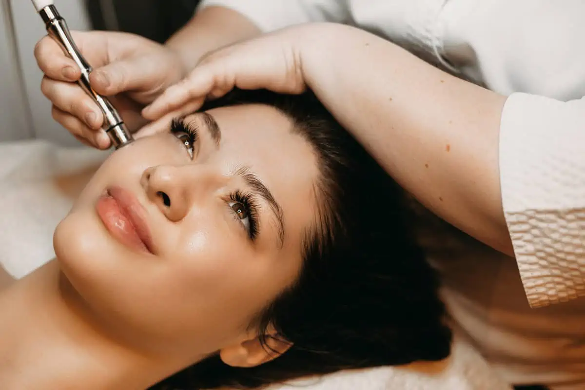 Gloved professional uses microneedling device on a woman’s face in Powell, WY.