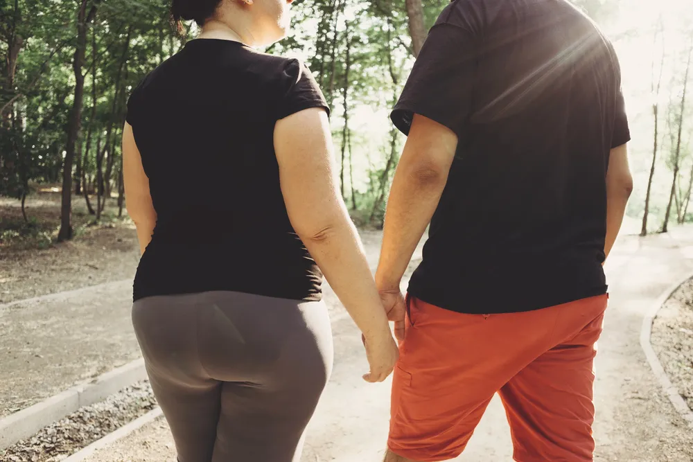 Couple in activewear holds hands while walking on a tree-lined path, promoting weight loss and healthy living in Powell, WY.