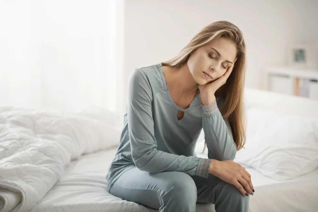 Woman sitting on bed looking tired and experiencing fatigue